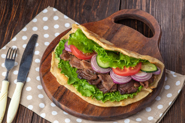 Delicious fresh homemade sandwich with chicken burspit roasted meat, tomato, onions and lettuce on wooden board on dark wooden table. Doner kebab. Healthy food concept.
