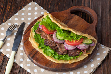 Delicious fresh homemade sandwich with chicken burspit roasted meat, tomato, onions and lettuce on wooden board on dark wooden table. Doner kebab. Healthy food concept.