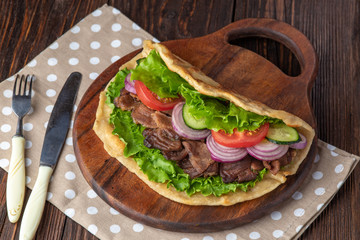 Delicious fresh homemade sandwich with chicken burspit roasted meat, tomato, onions and lettuce on wooden board on dark wooden table. Doner kebab. Healthy food concept.