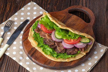 Delicious fresh homemade sandwich with chicken burspit roasted meat, tomato, onions and lettuce on wooden board on dark wooden table. Doner kebab. Healthy food concept.