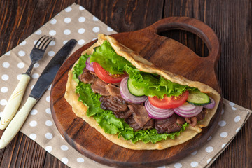 Delicious fresh homemade sandwich with chicken burspit roasted meat, tomato, onions and lettuce on wooden board on dark wooden table. Doner kebab. Healthy food concept.