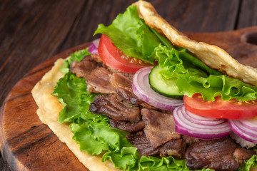 Delicious fresh homemade sandwich with chicken burspit roasted meat, tomato, onions and lettuce on wooden board on dark wooden table. Doner kebab. Healthy food concept.