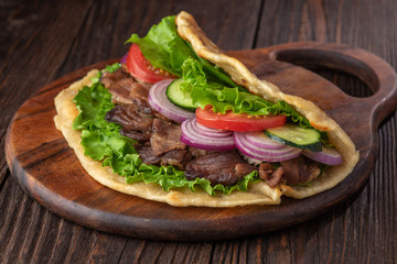 Delicious fresh homemade sandwich with chicken burspit roasted meat, tomato, onions and lettuce on wooden board on dark wooden table. Doner kebab. Healthy food concept.