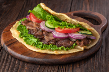 Delicious fresh homemade sandwich with chicken burspit roasted meat, tomato, onions and lettuce on wooden board on dark wooden table. Doner kebab. Healthy food concept.