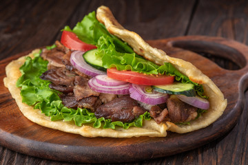 Delicious fresh homemade sandwich with chicken burspit roasted meat, tomato, onions and lettuce on wooden board on dark wooden table. Doner kebab. Healthy food concept.