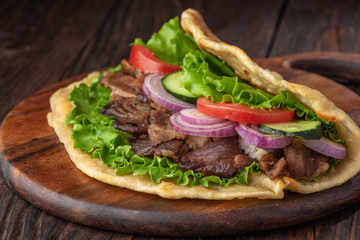 Delicious fresh homemade sandwich with chicken burspit roasted meat, tomato, onions and lettuce on wooden board on dark wooden table. Doner kebab. Healthy food concept.