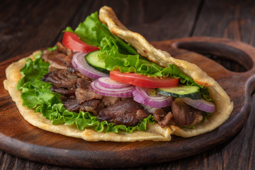 Delicious fresh homemade sandwich with chicken burspit roasted meat, tomato, onions and lettuce on wooden board on dark wooden table. Doner kebab. Healthy food concept.