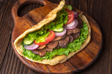 Delicious fresh homemade sandwich with chicken burspit roasted meat, tomato, onions and lettuce on wooden board on dark wooden table. Doner kebab. Healthy food concept.