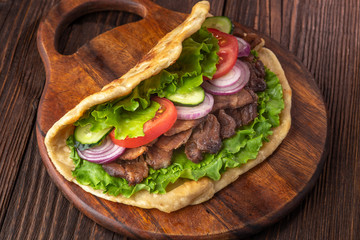 Delicious fresh homemade sandwich with chicken burspit roasted meat, tomato, onions and lettuce on wooden board on dark wooden table. Doner kebab. Healthy food concept.