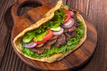 Delicious fresh homemade sandwich with chicken burspit roasted meat, tomato, onions and lettuce on wooden board on dark wooden table. Doner kebab. Healthy food concept.