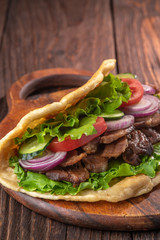 Delicious fresh homemade sandwich with chicken burspit roasted meat, tomato, onions and lettuce on wooden board on dark wooden table. Doner kebab. Healthy food concept.