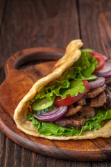 Delicious fresh homemade sandwich with chicken burspit roasted meat, tomato, onions and lettuce on wooden board on dark wooden table. Doner kebab. Healthy food concept.