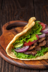 Delicious fresh homemade sandwich with chicken burspit roasted meat, tomato, onions and lettuce on wooden board on dark wooden table. Doner kebab. Healthy food concept.