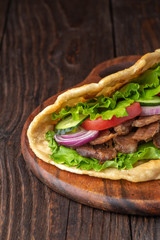 Delicious fresh homemade sandwich with chicken burspit roasted meat, tomato, onions and lettuce on wooden board on dark wooden table. Doner kebab. Healthy food concept.