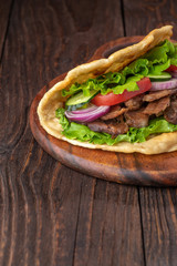 Delicious fresh homemade sandwich with chicken burspit roasted meat, tomato, onions and lettuce on wooden board on dark wooden table. Doner kebab. Healthy food concept.