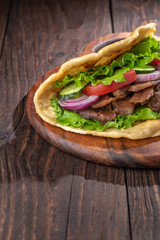 Delicious fresh homemade sandwich with chicken burspit roasted meat, tomato, onions and lettuce on wooden board on dark wooden table. Doner kebab. Healthy food concept.