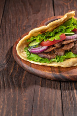 Delicious fresh homemade sandwich with chicken burspit roasted meat, tomato, onions and lettuce on wooden board on dark wooden table. Doner kebab. Healthy food concept.