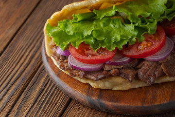 Delicious fresh homemade sandwich with chicken burspit roasted meat, tomato, onions and lettuce on wooden board on dark wooden table. Doner kebab. Healthy food concept.