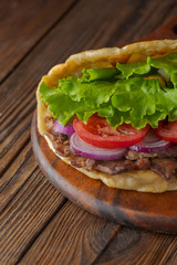 Delicious fresh homemade sandwich with chicken burspit roasted meat, tomato, onions and lettuce on wooden board on dark wooden table. Doner kebab. Healthy food concept.