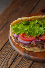 Delicious fresh homemade sandwich with chicken burspit roasted meat, tomato, onions and lettuce on wooden board on dark wooden table. Doner kebab. Healthy food concept.
