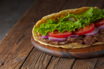 Delicious fresh homemade sandwich with chicken burspit roasted meat, tomato, onions and lettuce on wooden board on dark wooden table. Doner kebab. Healthy food concept.