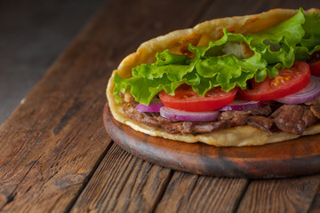 Delicious fresh homemade sandwich with chicken burspit roasted meat, tomato, onions and lettuce on wooden board on dark wooden table. Doner kebab. Healthy food concept.