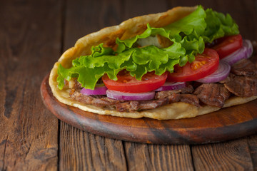 Delicious fresh homemade sandwich with chicken burspit roasted meat, tomato, onions and lettuce on wooden board on dark wooden table. Doner kebab. Healthy food concept.