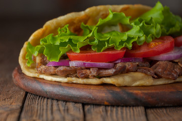 Delicious fresh homemade sandwich with chicken burspit roasted meat, tomato, onions and lettuce on wooden board on dark wooden table. Doner kebab. Healthy food concept.