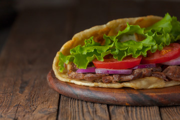 Delicious fresh homemade sandwich with chicken burspit roasted meat, tomato, onions and lettuce on wooden board on dark wooden table. Doner kebab. Healthy food concept.