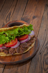 Delicious fresh homemade sandwich with chicken burspit roasted meat, tomato, onions and lettuce on wooden board on dark wooden table. Doner kebab. Healthy food concept.