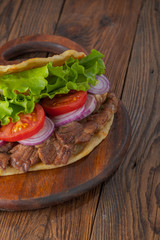 Delicious fresh homemade sandwich with chicken burspit roasted meat, tomato, onions and lettuce on wooden board on dark wooden table. Doner kebab. Healthy food concept.