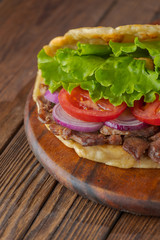 Delicious fresh homemade sandwich with chicken burspit roasted meat, tomato, onions and lettuce on wooden board on dark wooden table. Doner kebab. Healthy food concept.