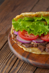 Delicious fresh homemade sandwich with chicken burspit roasted meat, tomato, onions and lettuce on wooden board on dark wooden table. Doner kebab. Healthy food concept.