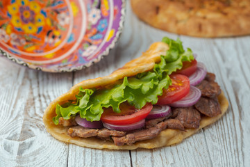 Delicious fresh homemade sandwich with chicken burspit roasted meat, tomato, onions and lettuce on wooden board on white wooden table. Doner kebab. Healthy food concept.