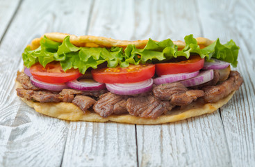 Delicious fresh homemade sandwich with chicken burspit roasted meat, tomato, onions and lettuce on wooden board on white wooden table. Doner kebab. Healthy food concept.