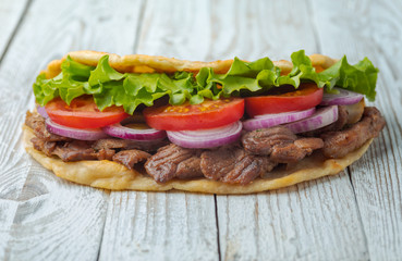 Delicious fresh homemade sandwich with chicken burspit roasted meat, tomato, onions and lettuce on wooden board on white wooden table. Doner kebab. Healthy food concept.