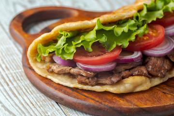 Delicious fresh homemade sandwich with chicken burspit roasted meat, tomato, onions and lettuce on wooden board on white wooden table. Doner kebab. Healthy food concept.
