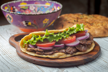 Delicious fresh homemade sandwich with chicken burspit roasted meat, tomato, onions and lettuce on wooden board on white wooden table. Doner kebab. Healthy food concept.
