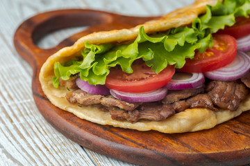 Delicious fresh homemade sandwich with chicken burspit roasted meat, tomato, onions and lettuce on wooden board on white wooden table. Doner kebab. Healthy food concept.