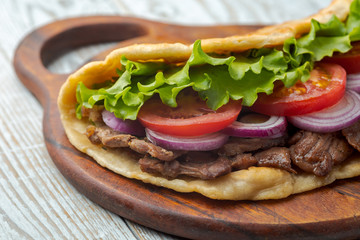 Delicious fresh homemade sandwich with chicken burspit roasted meat, tomato, onions and lettuce on wooden board on white wooden table. Doner kebab. Healthy food concept.