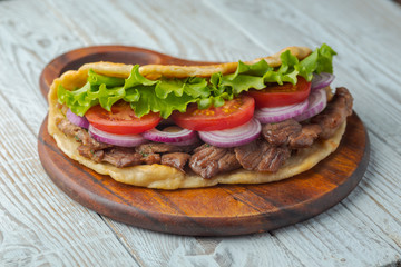 Delicious fresh homemade sandwich with chicken burspit roasted meat, tomato, onions and lettuce on wooden board on white wooden table. Doner kebab. Healthy food concept.