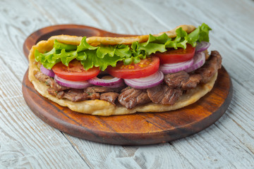 Delicious fresh homemade sandwich with chicken burspit roasted meat, tomato, onions and lettuce on wooden board on white wooden table. Doner kebab. Healthy food concept.