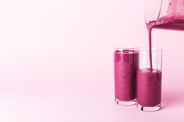 Two glasses of blueberries smoothie on pink background. Poring from blender into glass.
