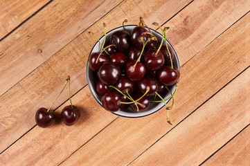 Cherries in a white bowl and a two cherries in front, on a wooden background
