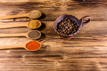 Ceramic bowl and spoons with the different spices on wooden table
