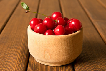 Ripe red cherry in a wooden plate on an old wooden table. The concept of natural food
