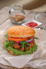 The hamburger lies on an old wooden table. On the table is a hamburger, tomato sauce, cherry tomatoes, a jar of spices.