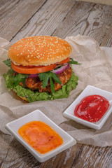 The hamburger lies on an old wooden table. On the table is a hamburger, tomato sauce, cherry tomatoes, a jar of spices.
