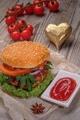 The hamburger lies on an old wooden table. On the table is a hamburger, tomato sauce, cherry tomatoes, a jar of spices.