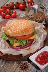The hamburger lies on an old wooden table. On the table is a hamburger, tomato sauce, cherry tomatoes, a jar of spices.